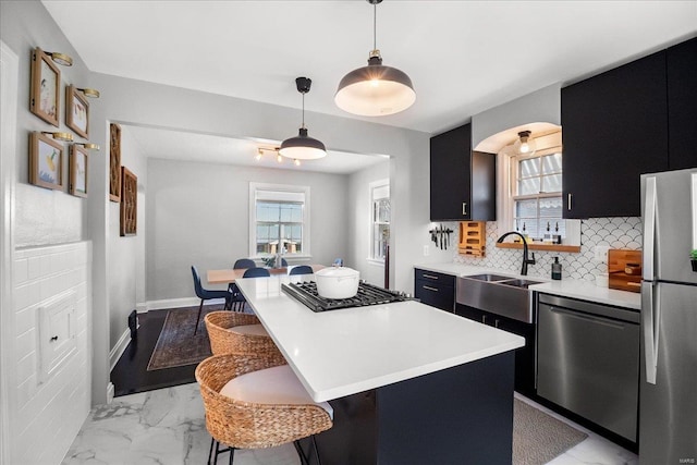 kitchen featuring appliances with stainless steel finishes, a sink, dark cabinetry, a kitchen breakfast bar, and light countertops