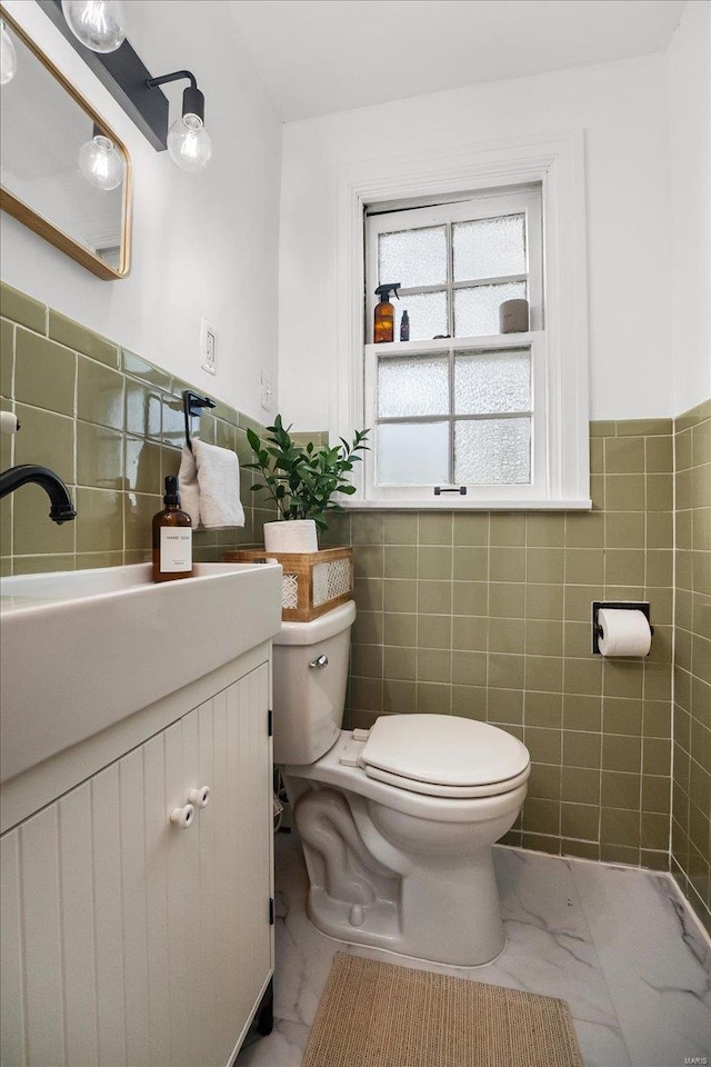 bathroom featuring vanity, a wainscoted wall, toilet, and tile walls