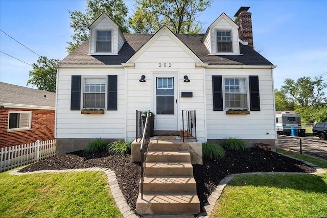 cape cod house featuring a shingled roof, fence, a front yard, and a chimney