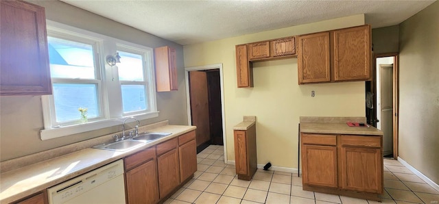 kitchen featuring light tile patterned floors, brown cabinets, dishwasher, a sink, and a textured ceiling