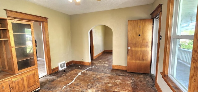 spare room with a textured ceiling, ceiling fan, visible vents, baseboards, and arched walkways