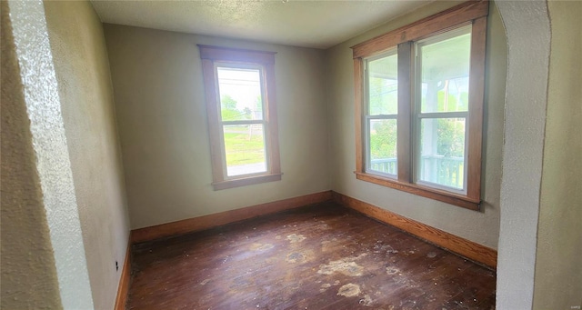 empty room featuring wood-type flooring, a textured wall, and baseboards