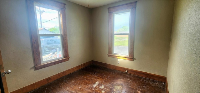 spare room featuring a textured wall, dark wood finished floors, and baseboards