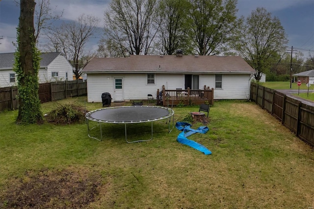 rear view of house with a fenced backyard, a trampoline, a wooden deck, and a yard