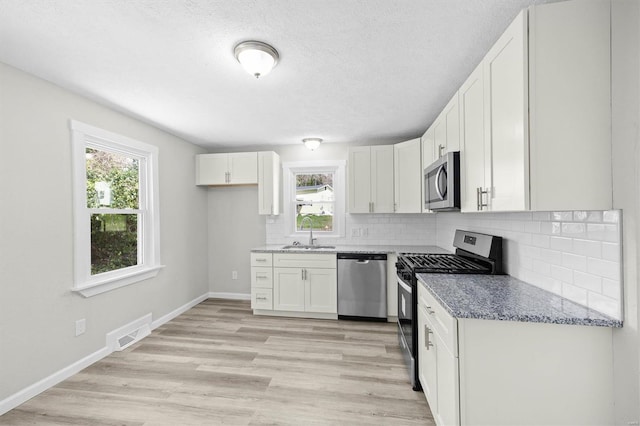 kitchen with appliances with stainless steel finishes, white cabinetry, a healthy amount of sunlight, and a sink