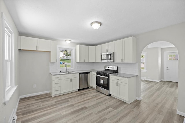 kitchen with stainless steel appliances, backsplash, arched walkways, and a sink