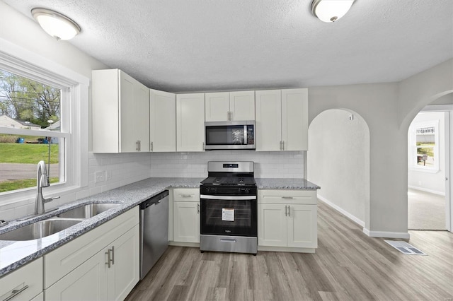 kitchen featuring arched walkways, a textured ceiling, appliances with stainless steel finishes, and a sink