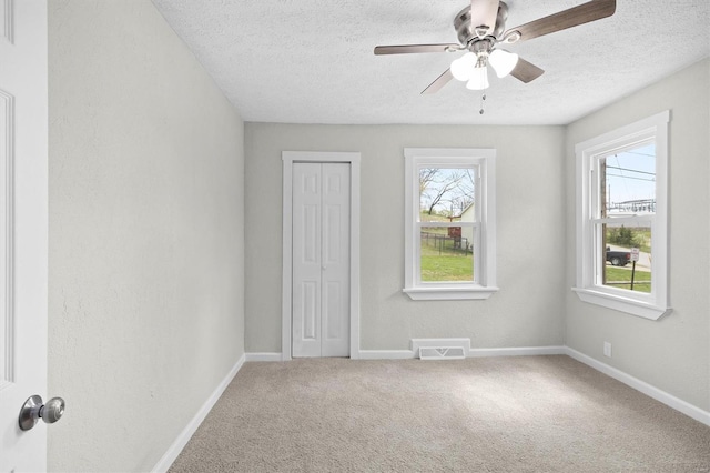 carpeted spare room with baseboards, visible vents, ceiling fan, and a textured ceiling