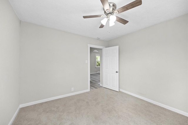 carpeted empty room featuring arched walkways, a textured ceiling, ceiling fan, and baseboards