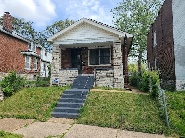 view of front of property with covered porch, brick siding, fence, stone siding, and a front yard