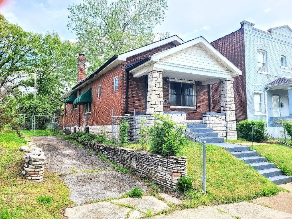 bungalow-style house featuring fence, a chimney, covered porch, and brick siding