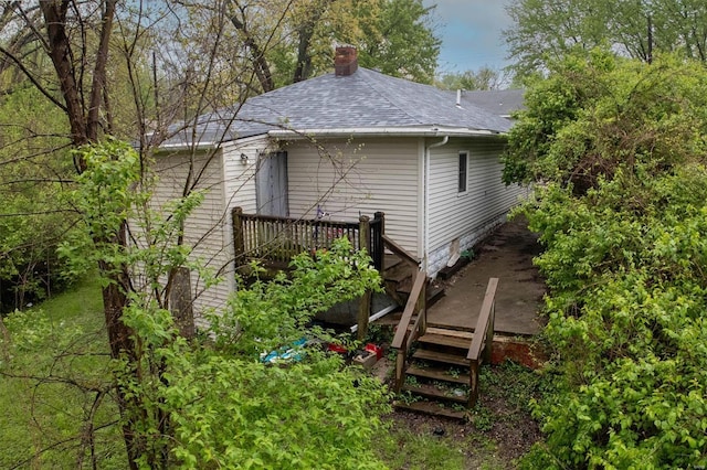 view of property exterior featuring roof with shingles, a chimney, and a deck