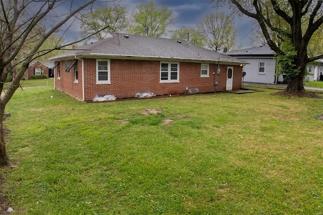 rear view of house featuring brick siding, a shingled roof, and a lawn