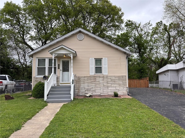 bungalow-style home featuring fence, central air condition unit, a front yard, and stone siding