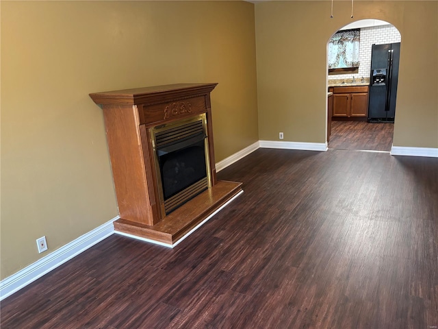 unfurnished living room featuring a fireplace with raised hearth, baseboards, a sink, and dark wood-type flooring