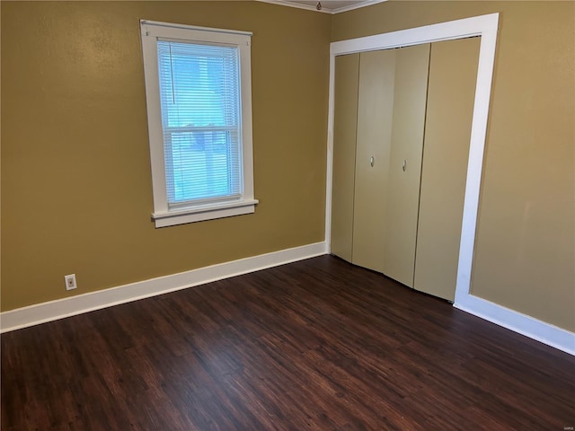 unfurnished bedroom featuring crown molding, a closet, baseboards, and dark wood-type flooring