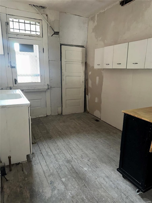 kitchen with a healthy amount of sunlight, white cabinets, light wood finished floors, and a sink