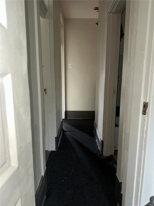 corridor with baseboards and dark carpet