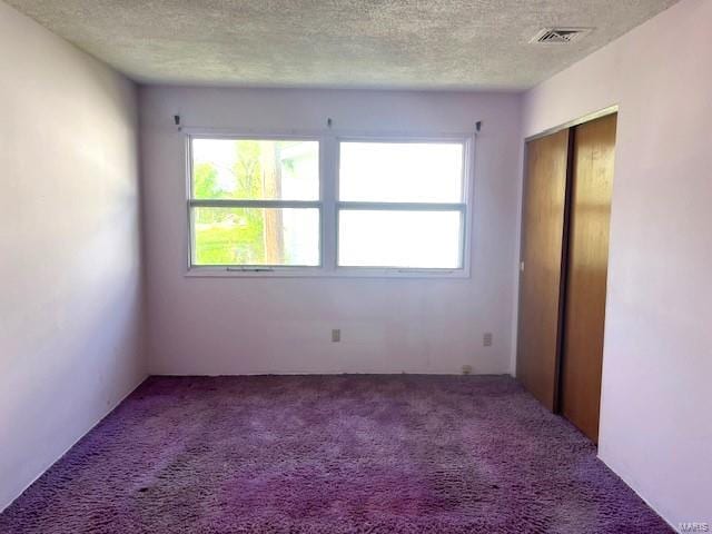 carpeted empty room with a textured ceiling and visible vents