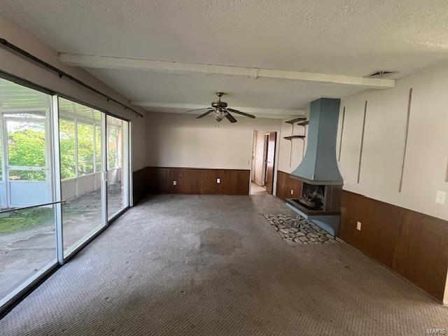 unfurnished living room with wainscoting, a textured ceiling, carpet, ceiling fan, and wooden walls