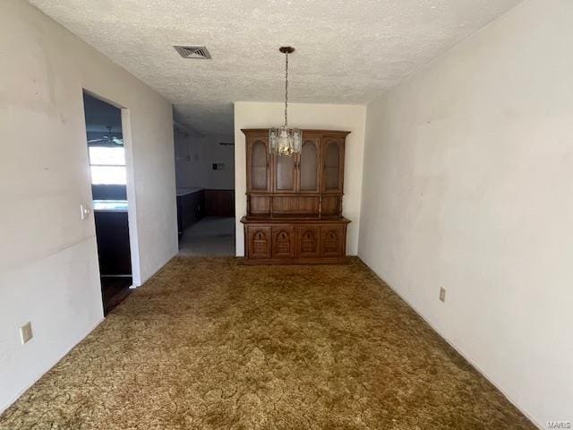 unfurnished dining area featuring carpet flooring, a textured ceiling, visible vents, and an inviting chandelier