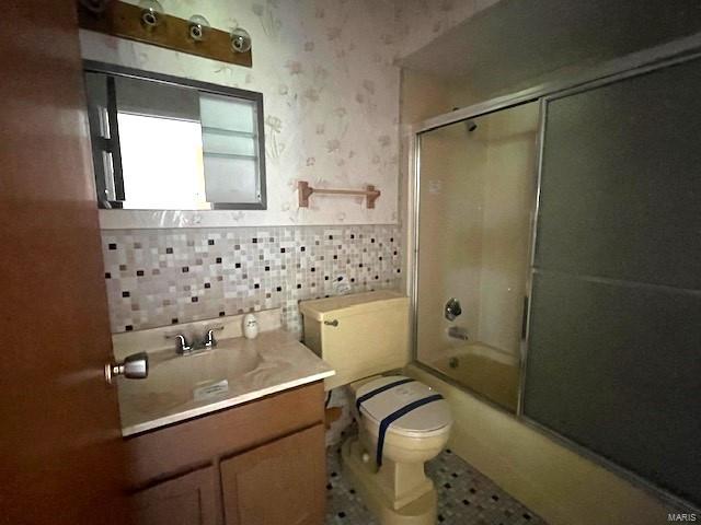 full bathroom featuring enclosed tub / shower combo, wallpapered walls, toilet, and vanity