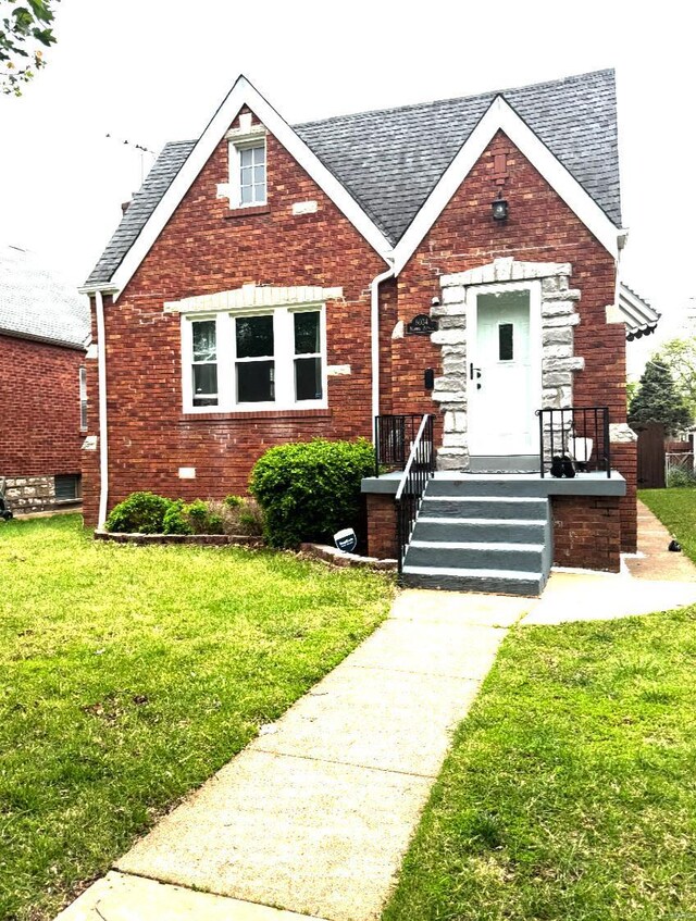 english style home with a front lawn, a shingled roof, and brick siding