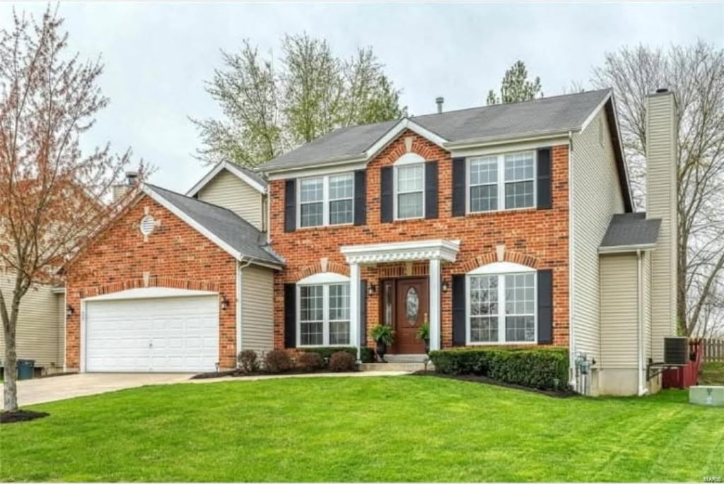 colonial home with a front yard, a garage, brick siding, driveway, and a chimney