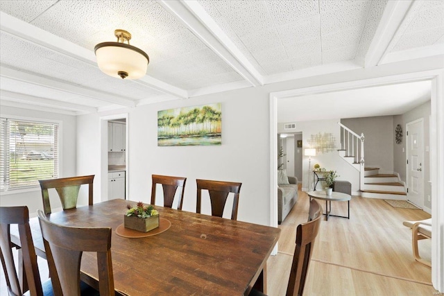 dining space featuring light wood-style floors, beamed ceiling, stairs, and visible vents