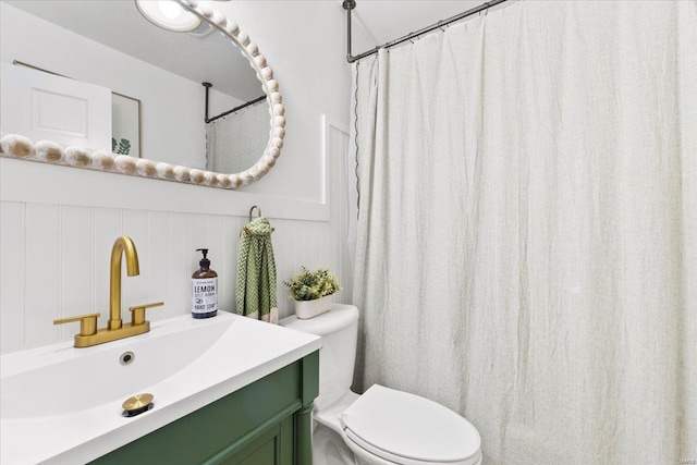 bathroom with a shower with curtain, vanity, a decorative wall, and toilet
