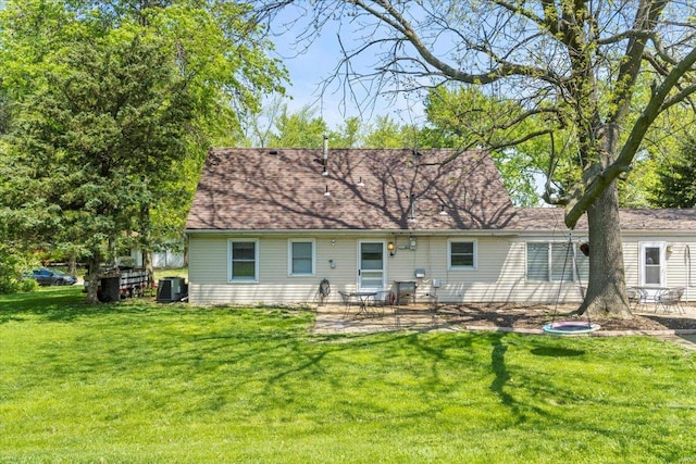 rear view of house with a lawn, central AC unit, a patio area, and roof with shingles