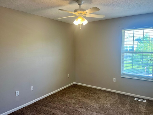 spare room featuring plenty of natural light, ceiling fan, visible vents, and dark colored carpet