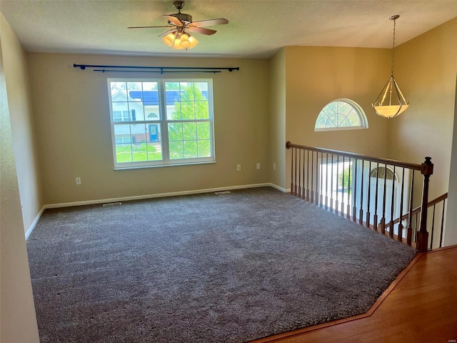 empty room featuring a textured ceiling, a ceiling fan, baseboards, wood finished floors, and visible vents