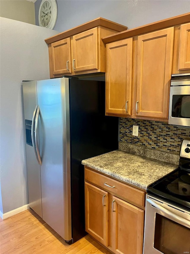 kitchen with light wood-style floors, appliances with stainless steel finishes, light stone counters, and backsplash