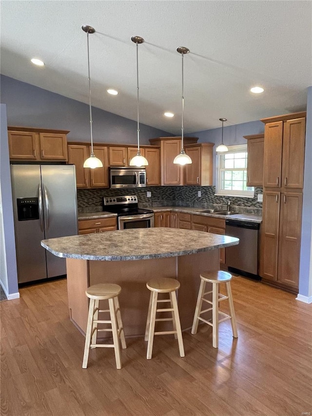 kitchen with appliances with stainless steel finishes, a kitchen breakfast bar, light wood-style flooring, a center island, and backsplash