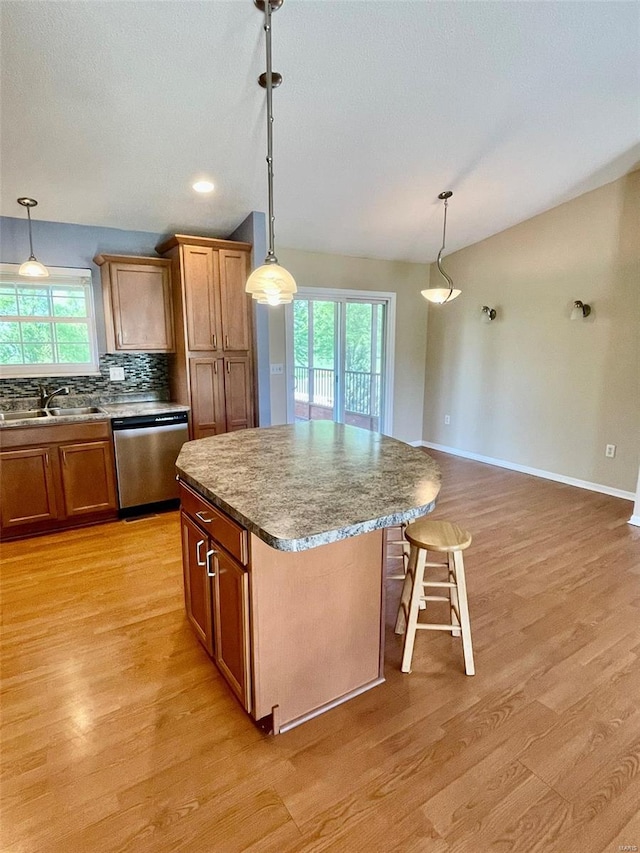 kitchen with stainless steel dishwasher, brown cabinetry, a sink, and light wood-style floors