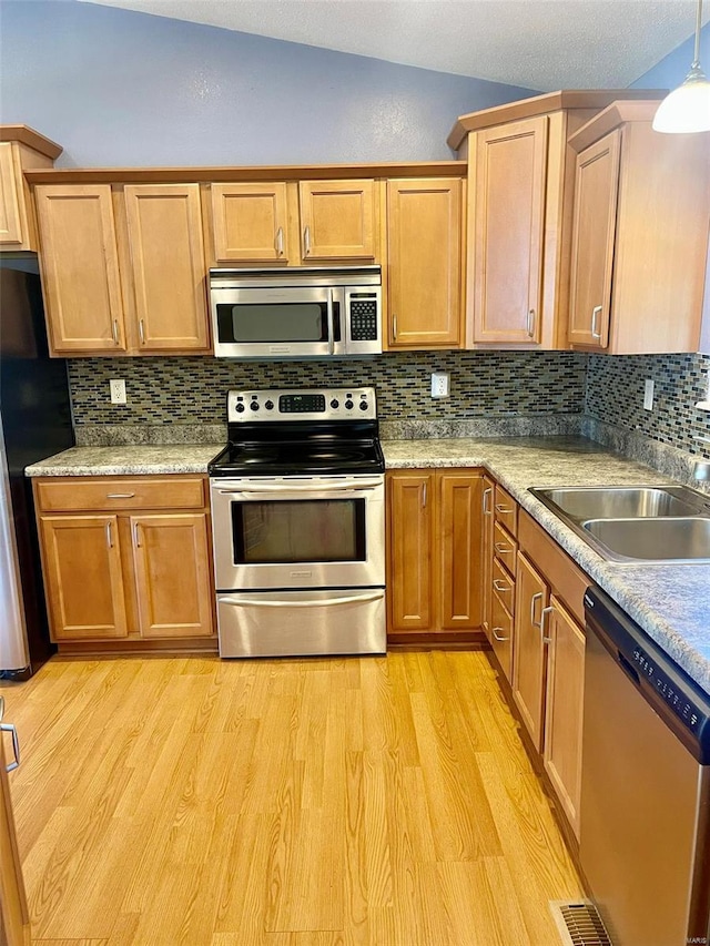 kitchen featuring backsplash, appliances with stainless steel finishes, vaulted ceiling, a sink, and light wood-style flooring