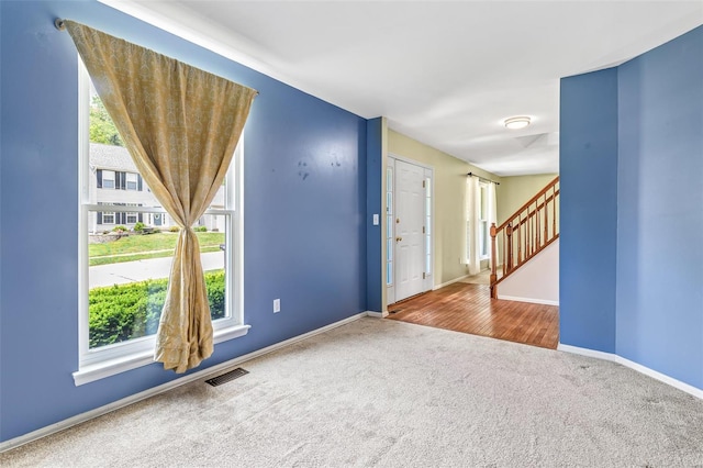 carpeted empty room featuring a healthy amount of sunlight, baseboards, stairs, and visible vents