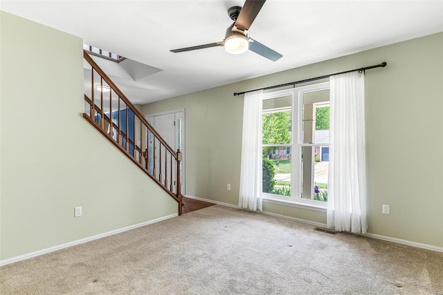 carpeted spare room featuring stairs, a ceiling fan, baseboards, and visible vents