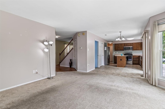 unfurnished living room with an inviting chandelier, baseboards, stairs, and light colored carpet