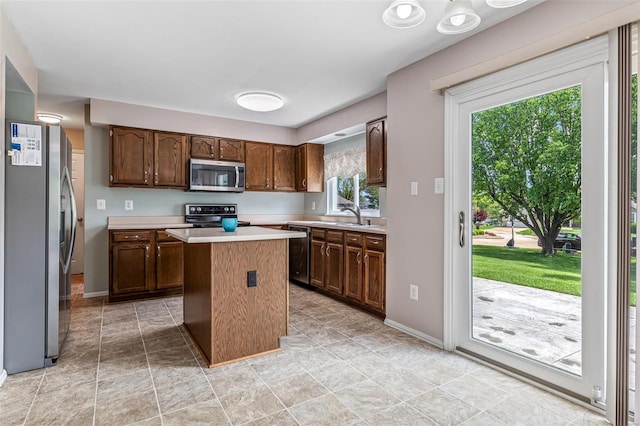 kitchen with a kitchen island, light countertops, baseboards, a sink, and stainless steel appliances