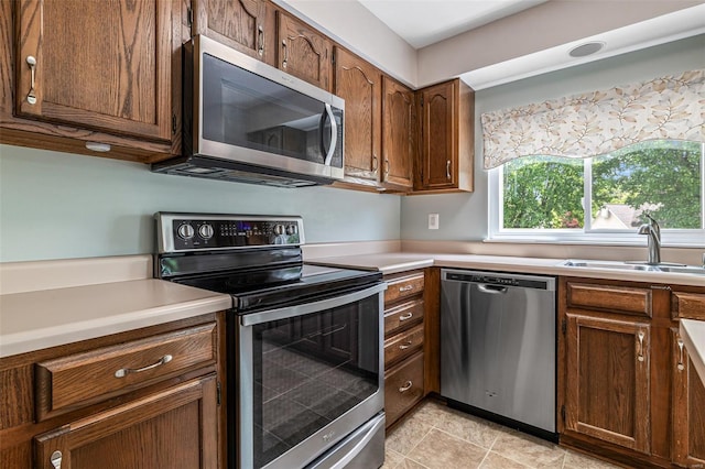 kitchen featuring light countertops, stainless steel appliances, brown cabinets, and a sink