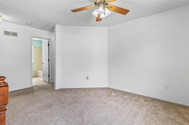 carpeted spare room with visible vents, attic access, baseboards, and a ceiling fan