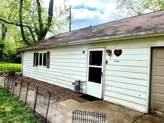 entrance to property with roof with shingles and fence