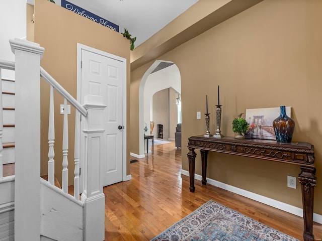entrance foyer with arched walkways, baseboards, stairway, and light wood-type flooring