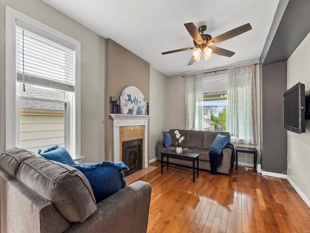 living area with baseboards, a fireplace, a ceiling fan, and hardwood / wood-style flooring