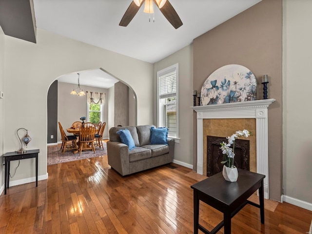 living room featuring a tiled fireplace, arched walkways, ceiling fan with notable chandelier, and hardwood / wood-style flooring