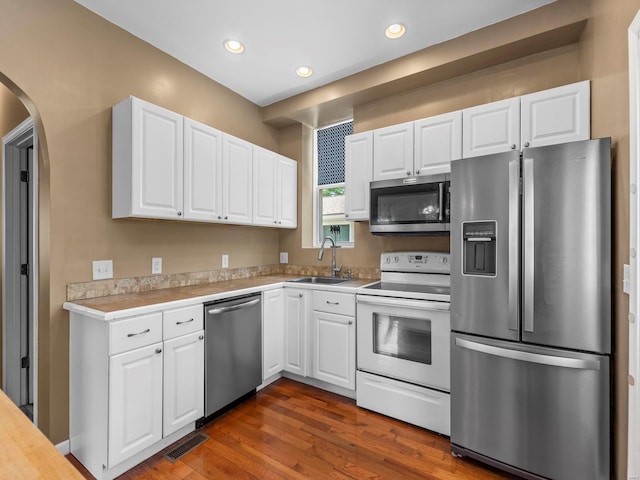 kitchen with arched walkways, a sink, light countertops, white cabinets, and stainless steel appliances