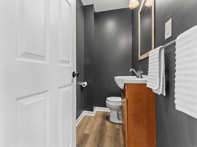 half bathroom featuring vanity, baseboards, wood finished floors, and toilet