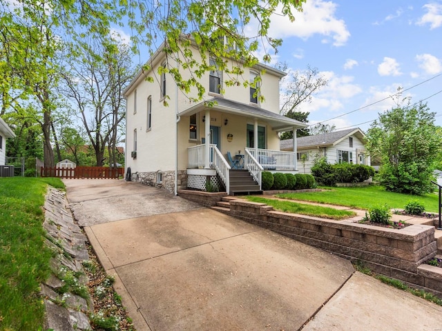 american foursquare style home with a front lawn, fence, covered porch, stucco siding, and concrete driveway